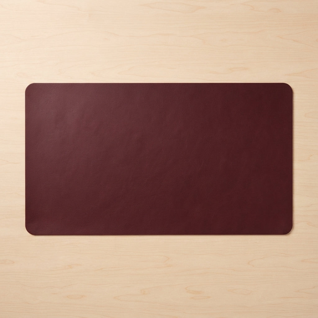 A dark burgundy rectangular desk mat with rounded corners, laid flat on a light wood grain surface.