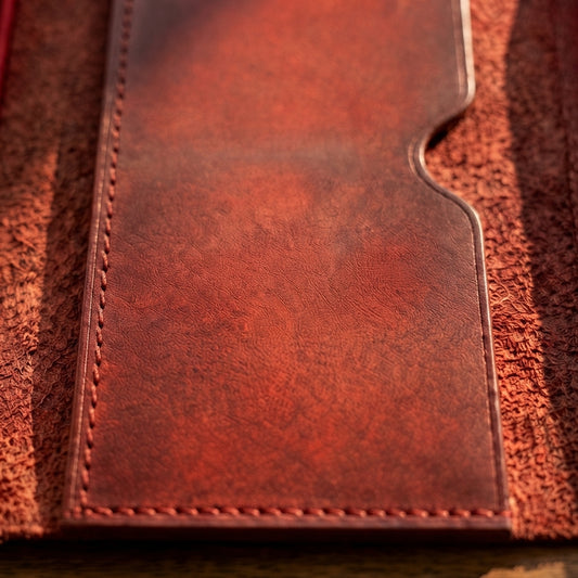 A close-up of a reddish-brown leather card holder or wallet sleeve with visible stitching and a textured finish, set against a matching brown textured background.