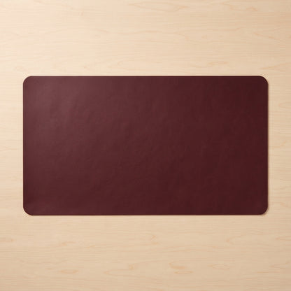 A dark burgundy rectangular desk mat with rounded corners, laid flat on a light wood grain surface.