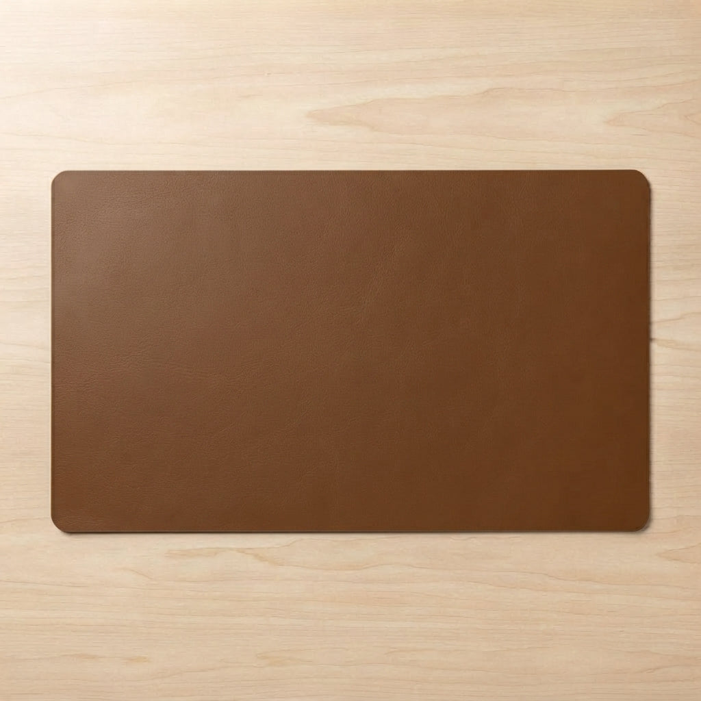 A rectangular brown leather desk mat with rounded corners, displayed flat on a light wood grain surface.