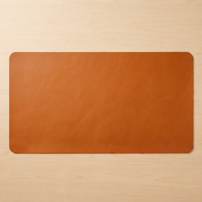 A rectangular tan leather desk mat with rounded corners, displayed flat on a light wood grain surface.