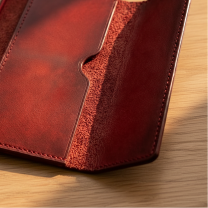 A dark red leather notebook cover or wallet shown open on a wooden surface, with a cream-colored notebook partially visible on the left.